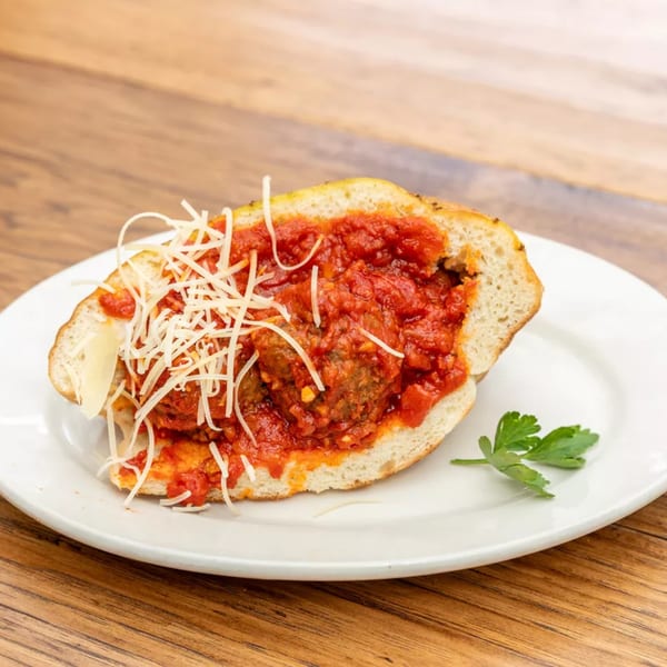 Meatball sub sandwich with marinara sauce and shredded cheese on a white plate with parsley.