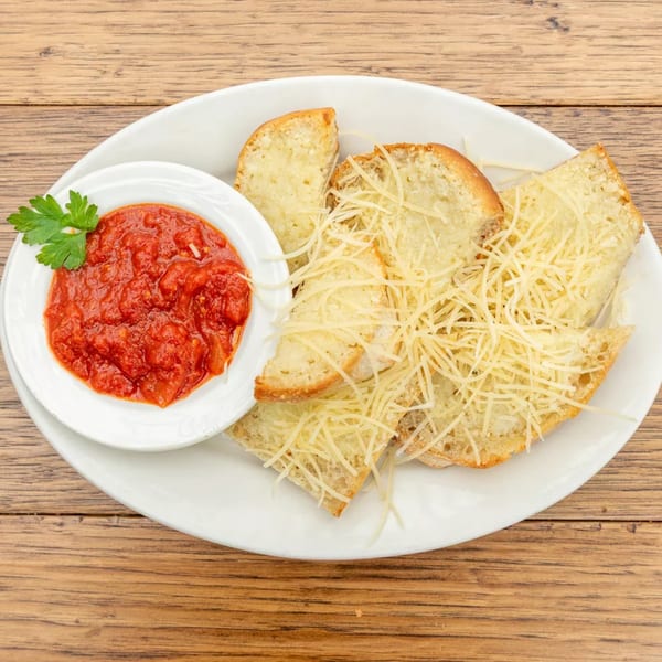 Garlic bread with shredded cheese and a side of marinara sauce on a white plate.