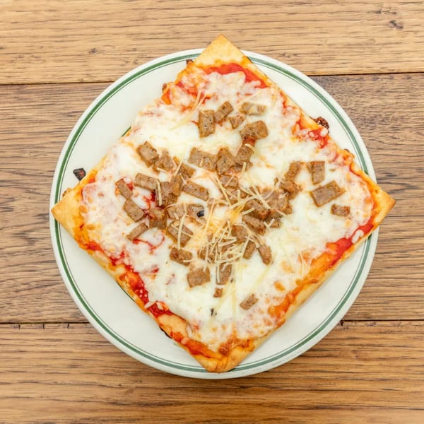 Square slice of pizza with melted cheese and sausage crumbles on a white plate with a green rim.