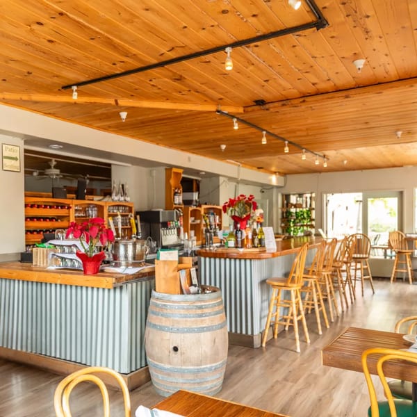 A rustic restaurant interior with a wooden ceiling, bar, and seating, featuring red floral arrangements.