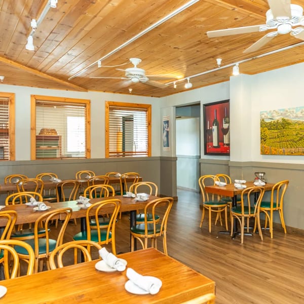 Empty restaurant dining room with wooden tables, chairs, and ceiling, featuring artwork on the walls.