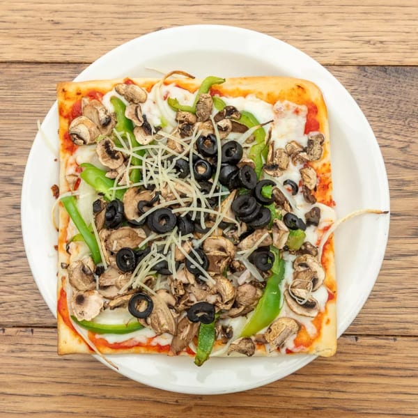 Square pizza with mushrooms, green peppers, black olives, and shredded cheese on a white plate.