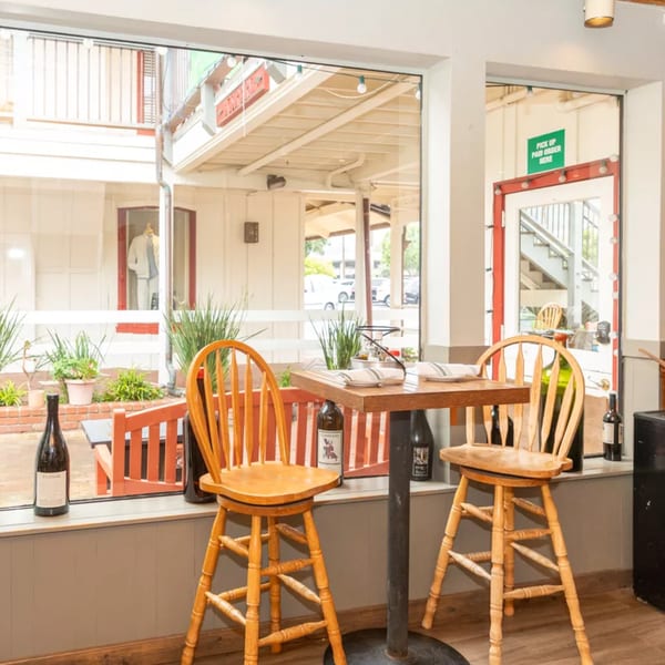 A cozy restaurant window table set for two with wine bottles, overlooking an outdoor patio.