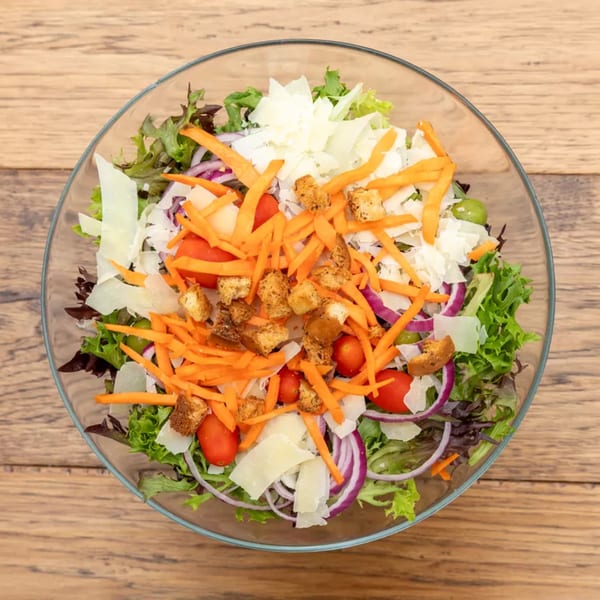Overhead view of a vibrant salad with mixed greens, carrots, tomatoes, red onion, croutons, and cheese.
