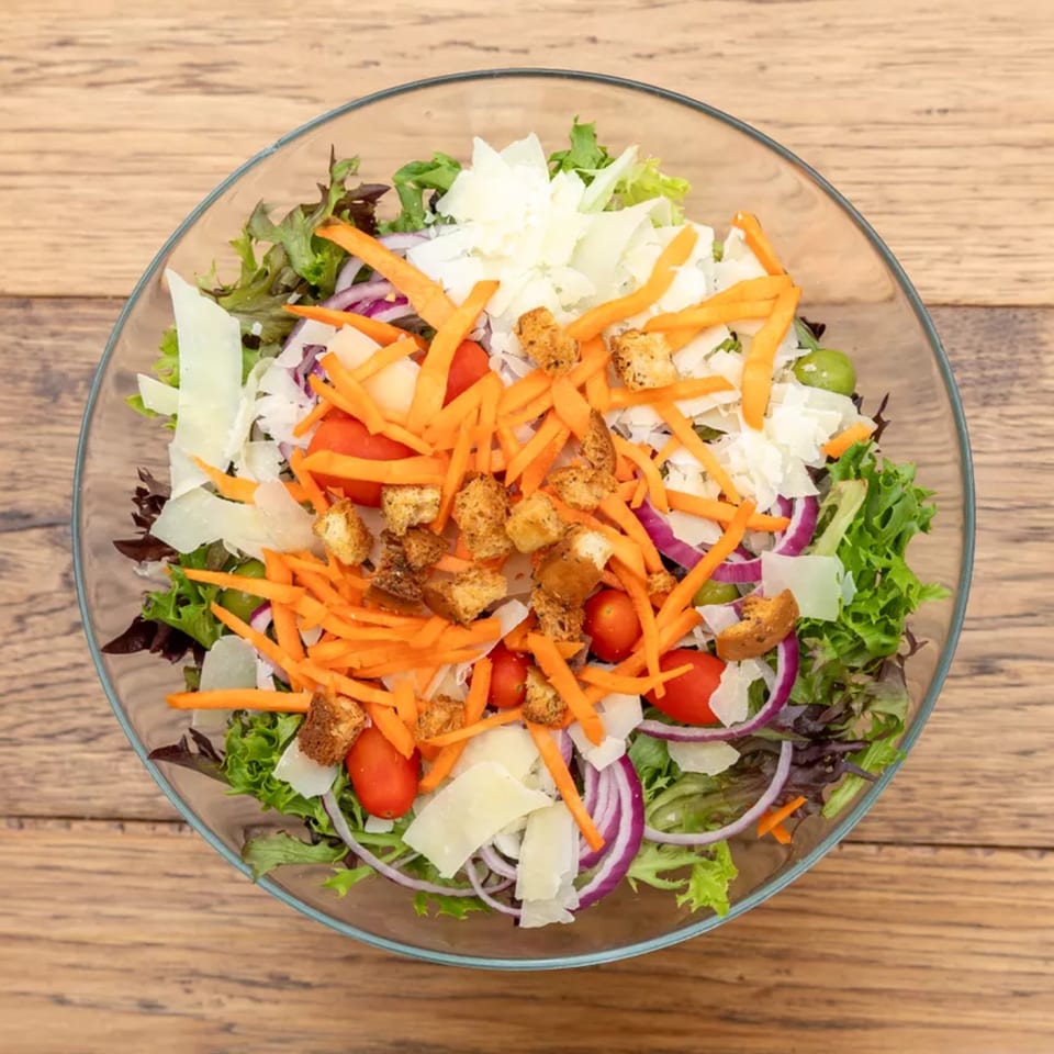 Overhead view of a vibrant salad with mixed greens, carrots, tomatoes, red onion, croutons, and cheese.