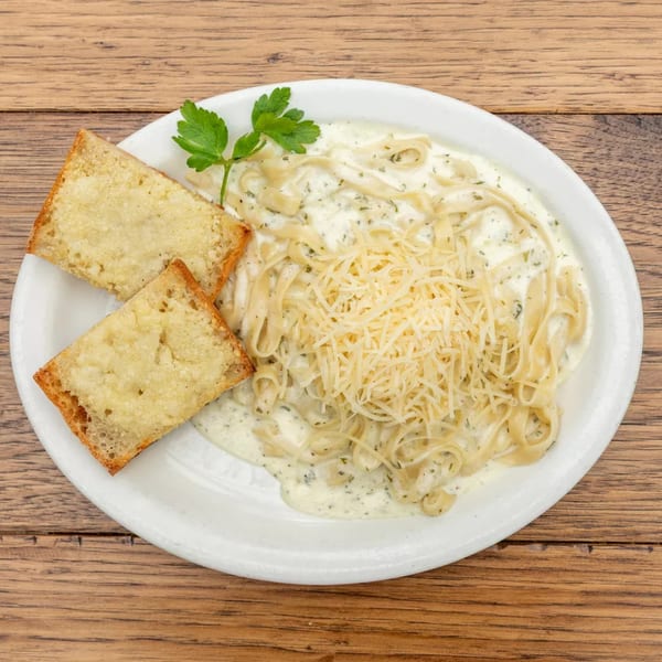 Creamy fettuccine alfredo pasta with shredded cheese, parsley, and two slices of garlic bread.