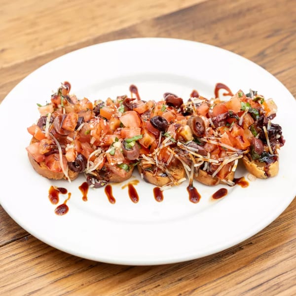 Bruschetta appetizers with diced tomatoes, olives, cheese, and balsamic glaze on a white plate.
