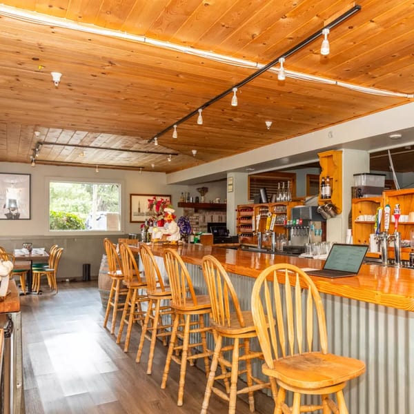Inviting restaurant interior with a long wooden bar, bar stools, and dining tables near a window.